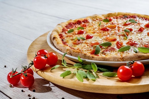 Nahaufnahme einer frisch gebackenen Pizza mit geschmolzenem Käse, Tomaten und Basilikum
